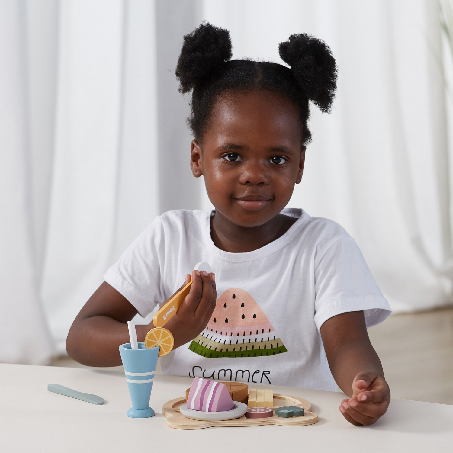 Criança a brincar com conjunto de brinquedo de comida em madeira e t-shirt branca com melancia e SUMMER.