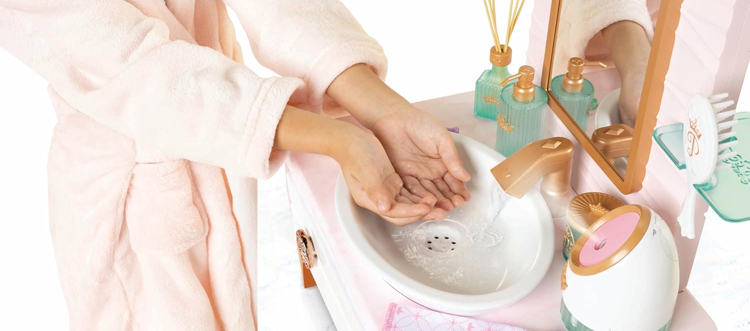 Pia infantil branca com dispenser dourado, frascos para sabonete e aromatizador verdes, escova pendurada e espelho com moldura dourada