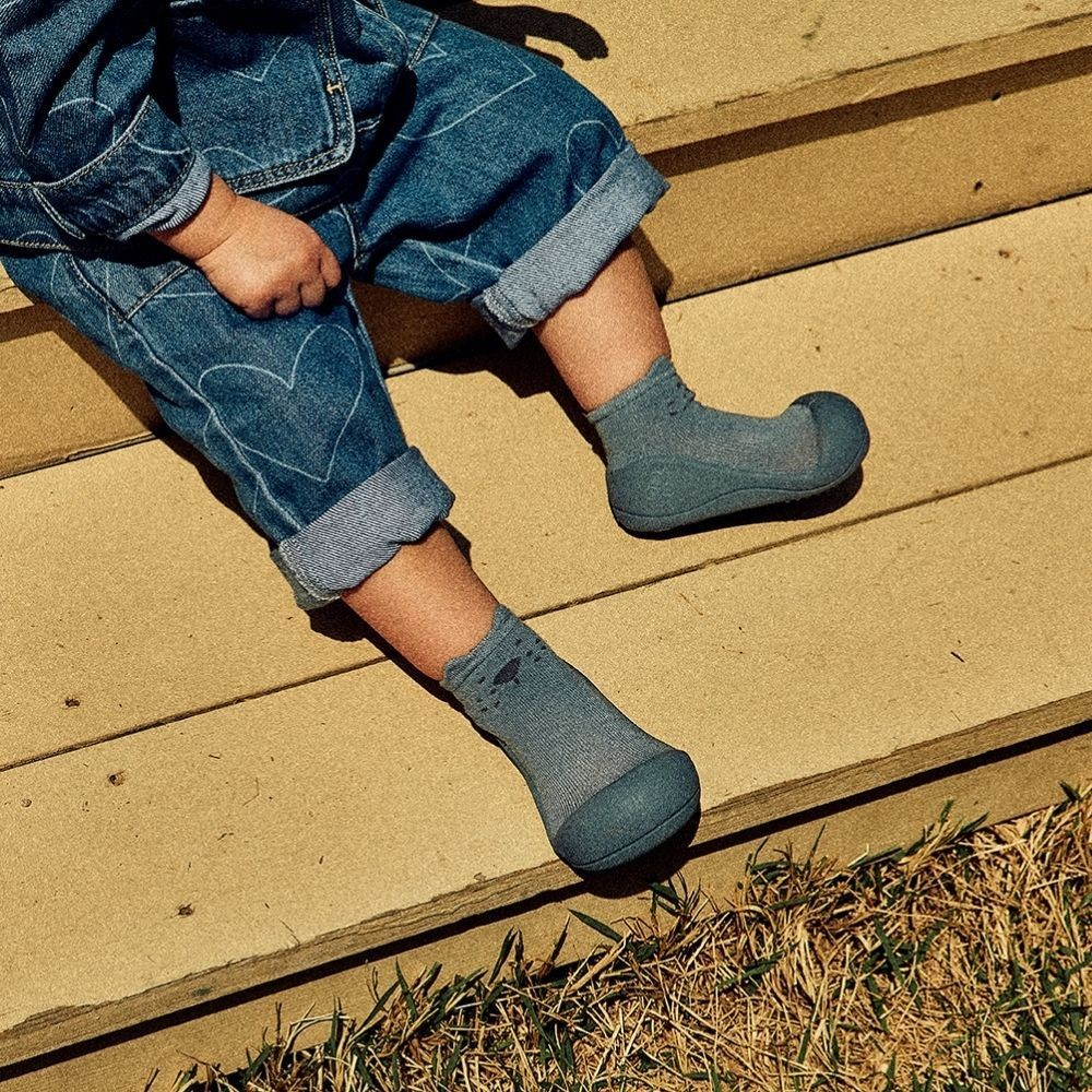 Criança com meias azuis com sola preta e calças de ganga sentada em escadas exteriores bege.