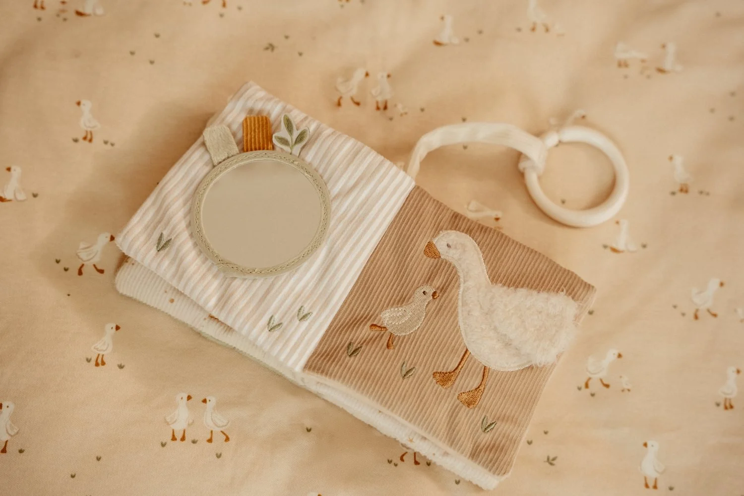 Livro macio em tecido com motivos de patos bordados e espelho redondo