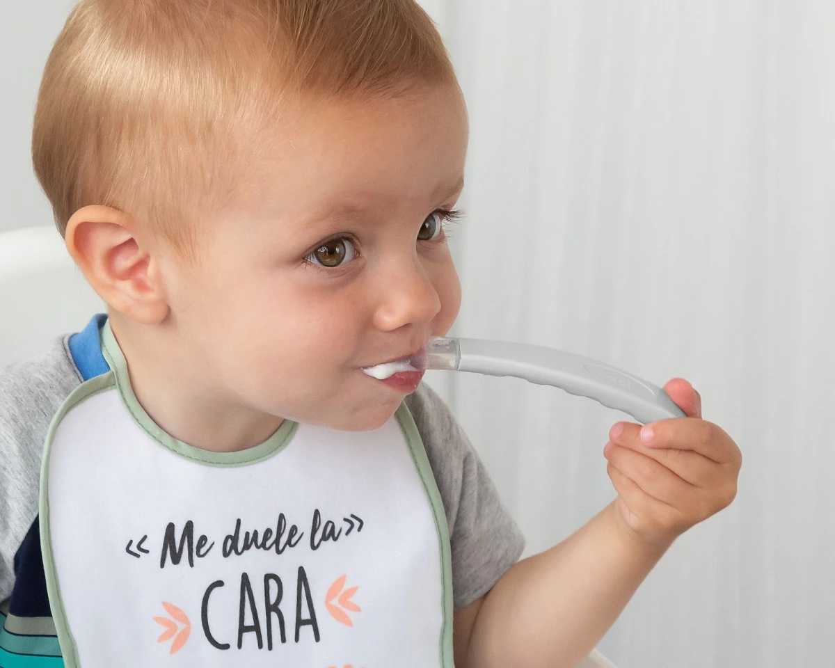 Criança com babete branco e texto a comer com colher cinzenta