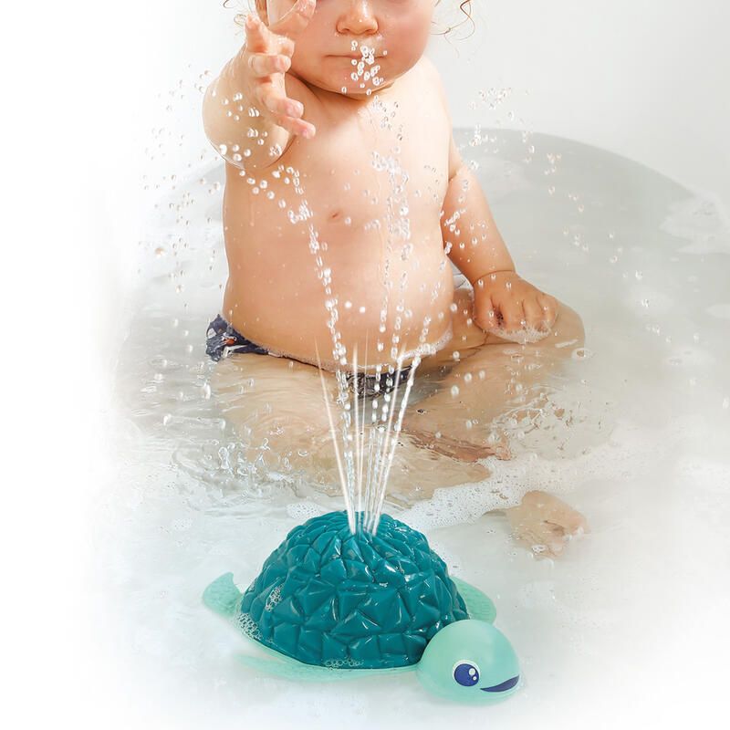 Brinquedo de banho tartaruga azul com água a sair, bebé ao fundo