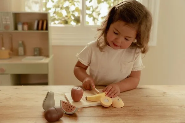 Criança a brincar com brinquedos de fruta de madeira numa mesa de madeira clara