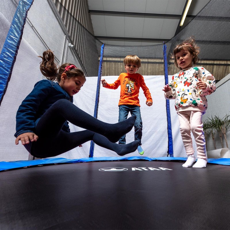 Três crianças a saltar num trampolim preto com estrutura azul e rede de proteção.