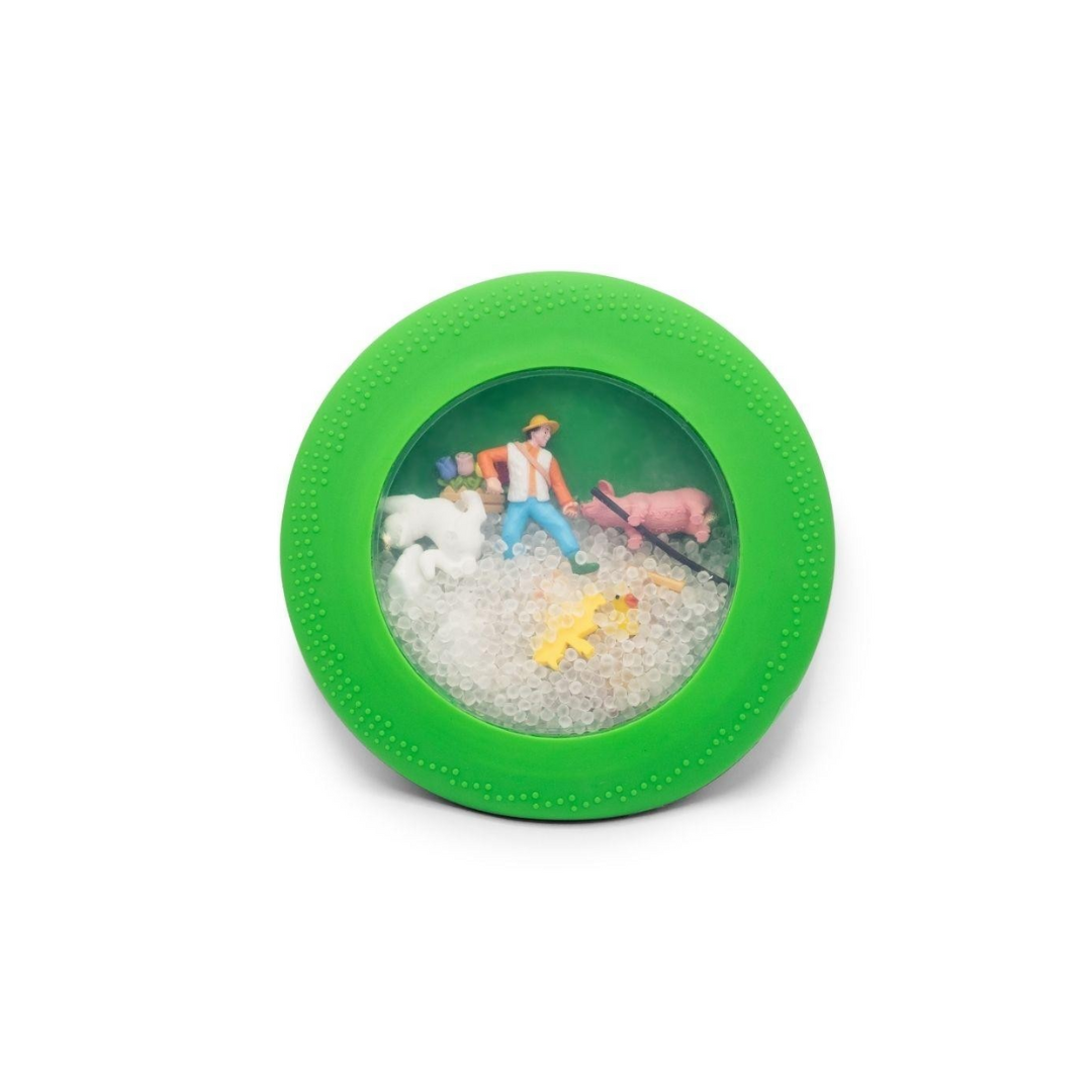 Brinquedo redondo verde com figuras de fazendeiro e animais numa janela transparente.