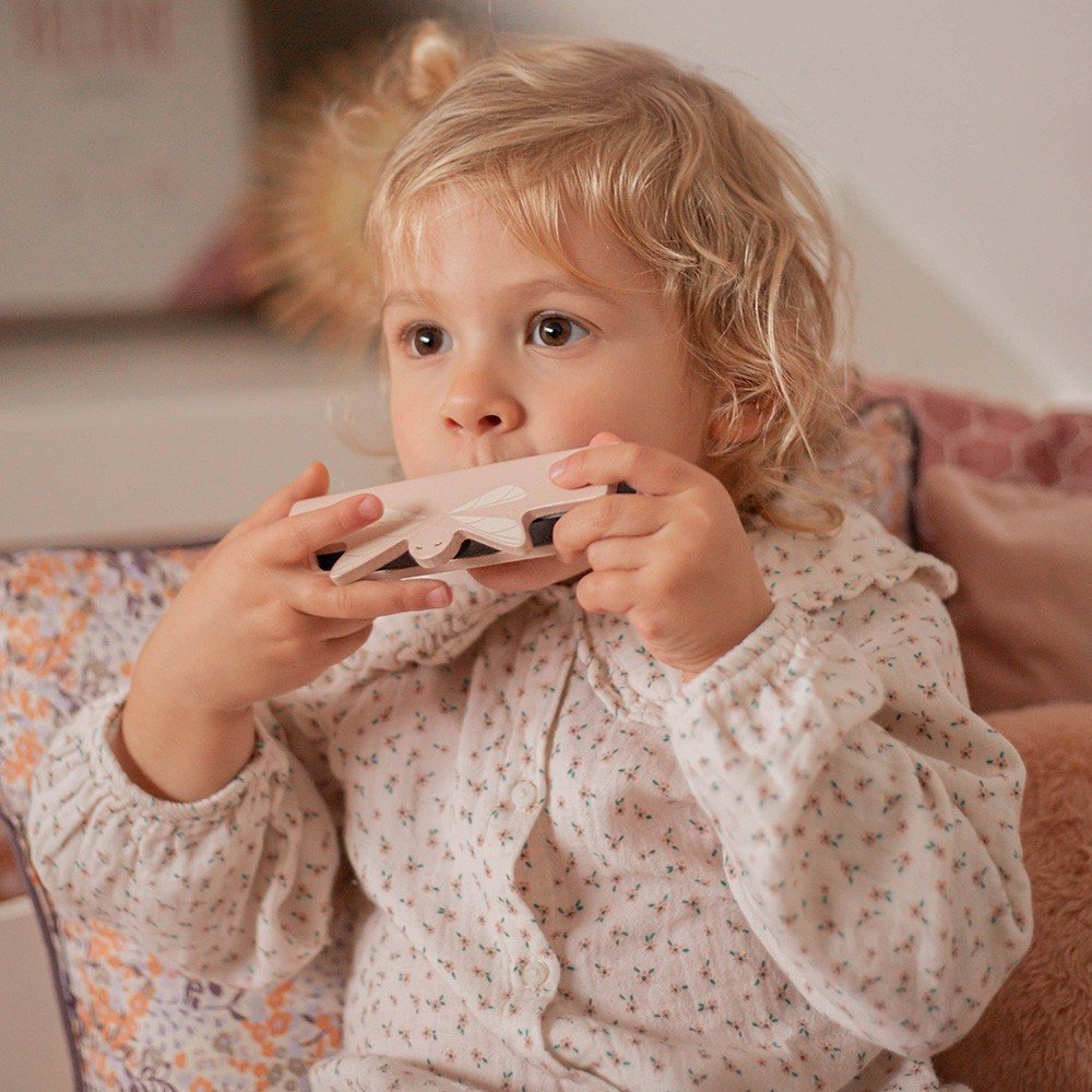 Criança loira a segurar brinquedo de madeira sentada num sofá com almofadas coloridas
