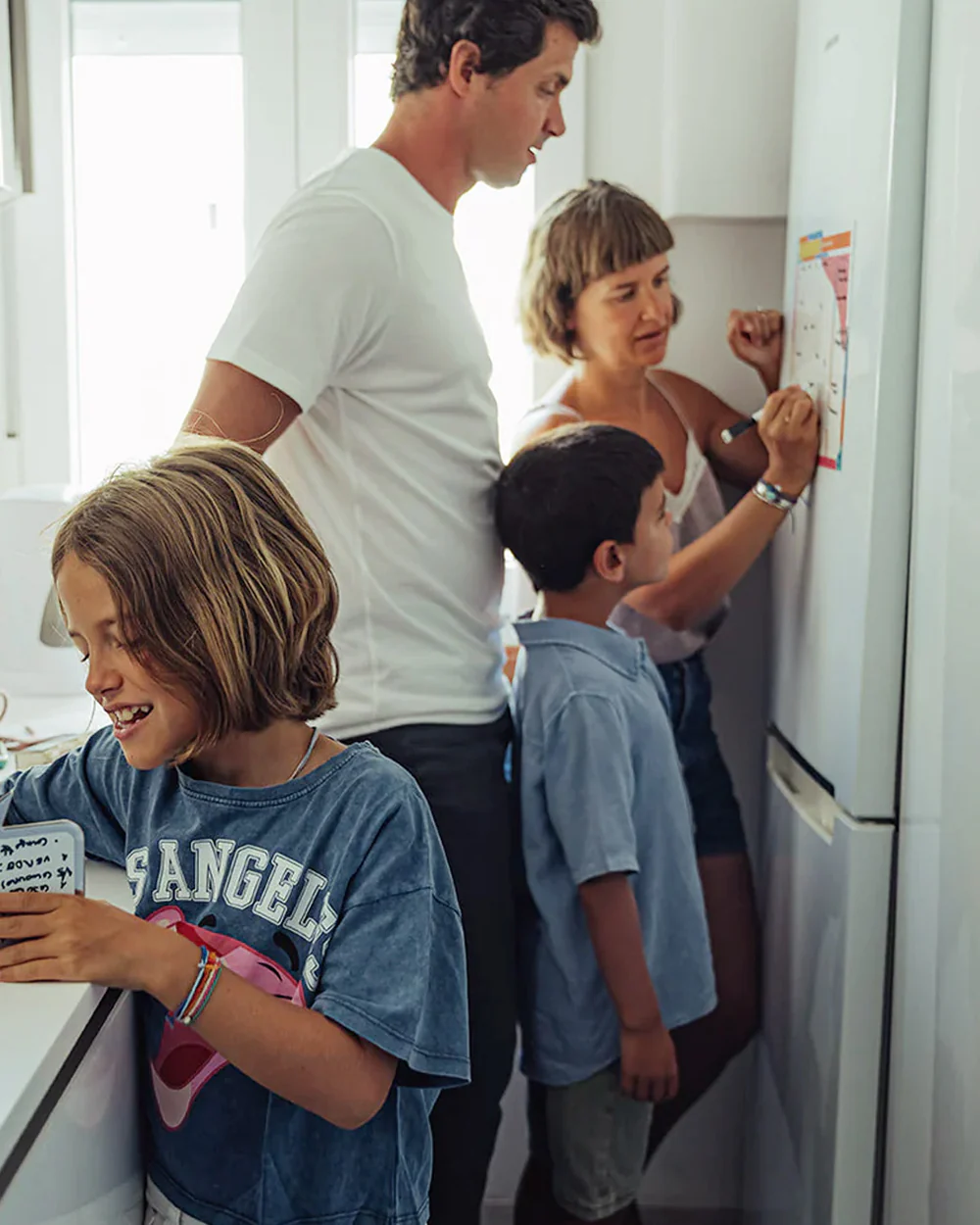 Família junta à frente de frigorífico branco, mulher escreve em papel colorido com marcador