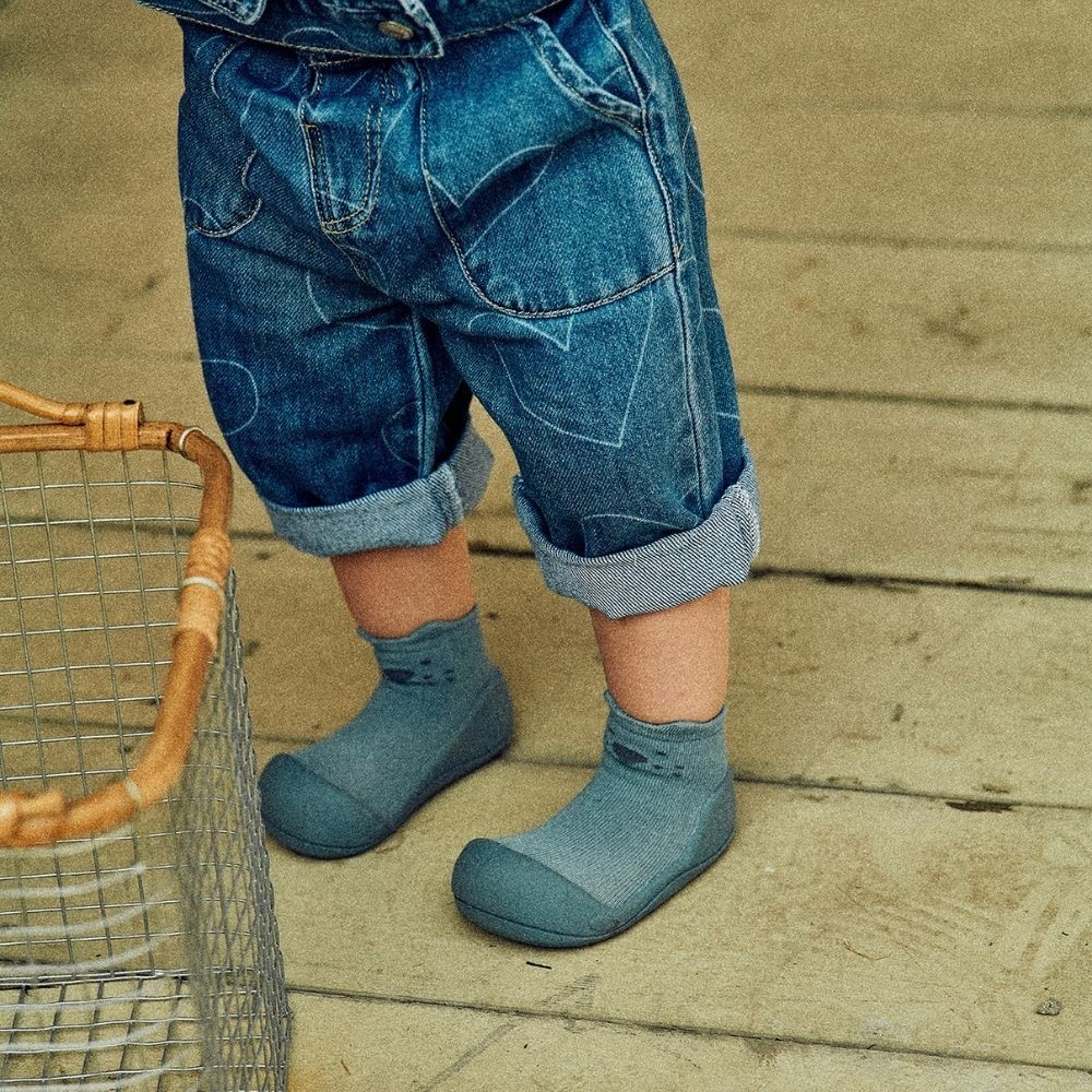 Sapatos infantis cinza-azulados com calças de ganga azuis e cesta metálica ao lado