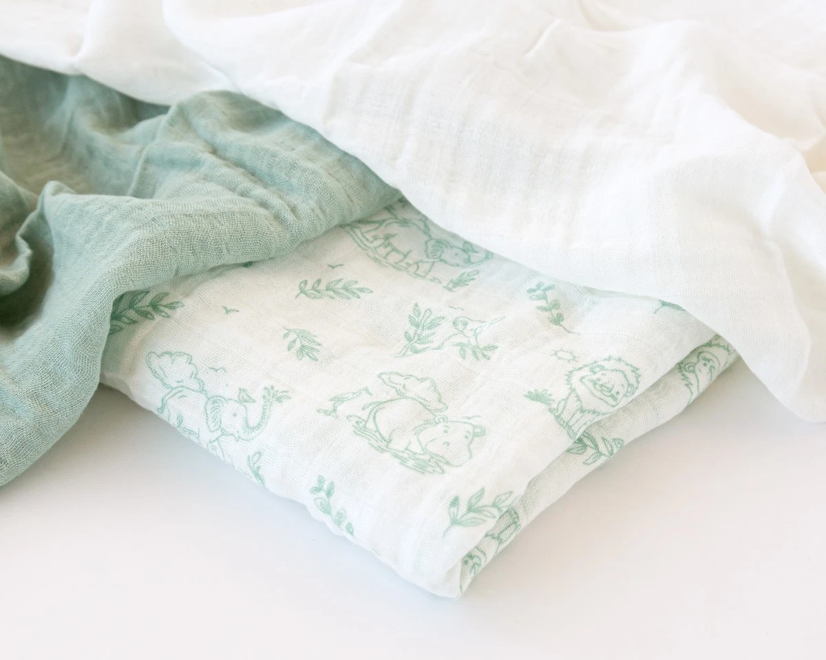 Tecidos de musselina em tons verde água e branco com padrão de animais.