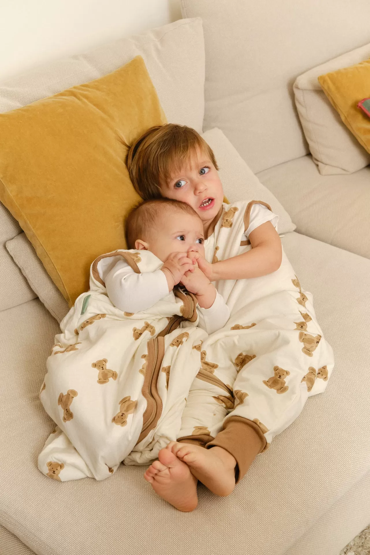 Dois bebés deitados em sofá com sacos de dormir com padrão de ursinhos