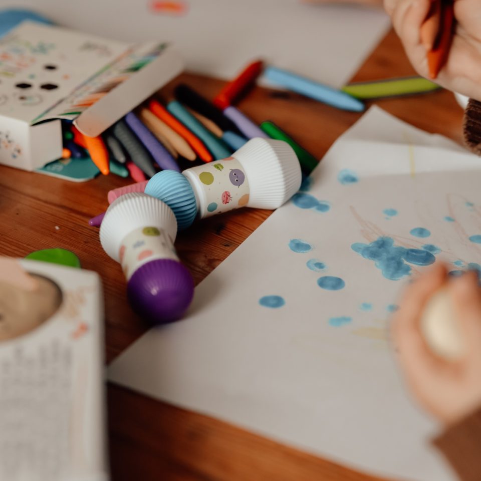 Giz de cera coloridos e carimbos de pintura sobre mesa de madeira com papel e manchas de tinta azul