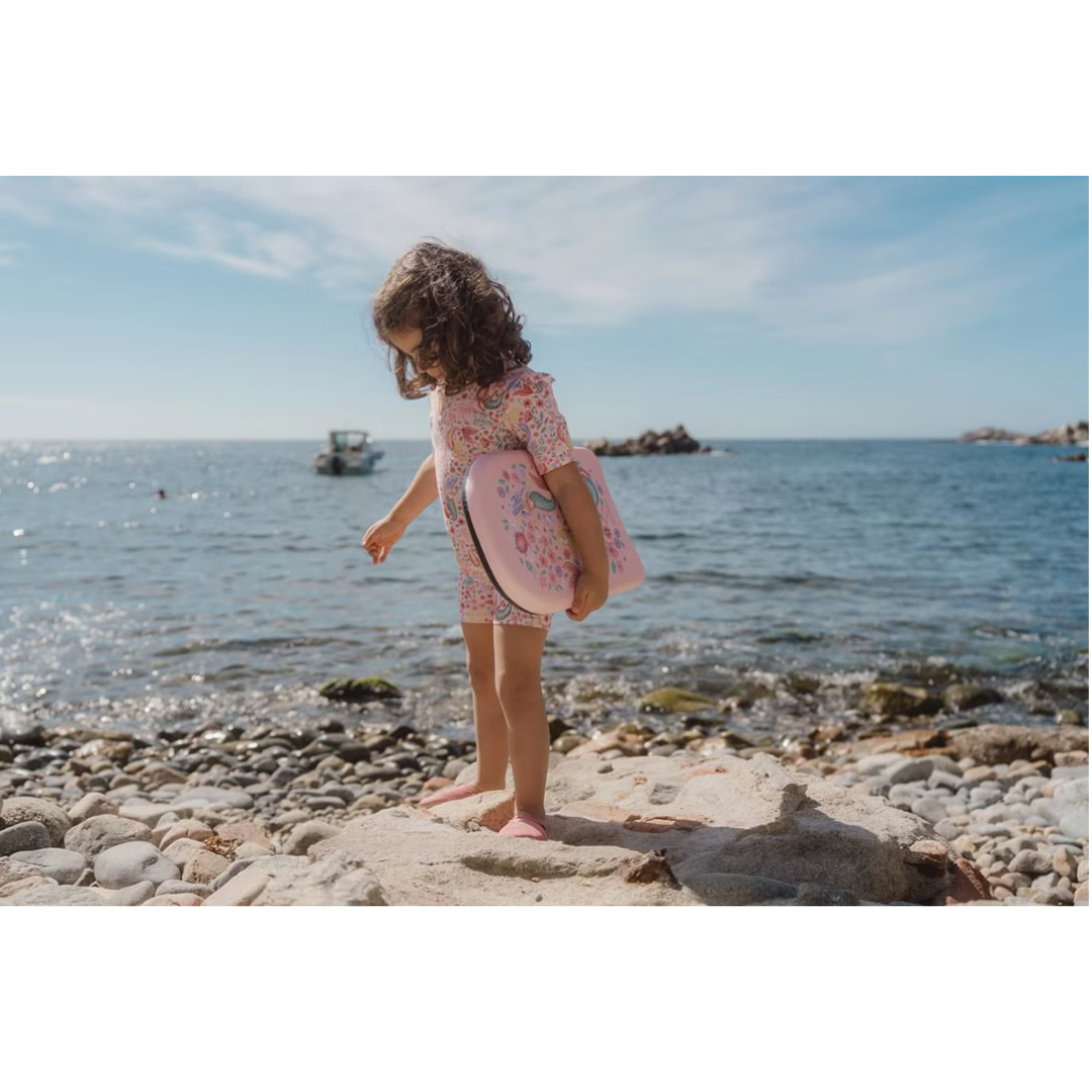 Criança com fato de banho e caixa floral junto ao mar numa praia de pedras