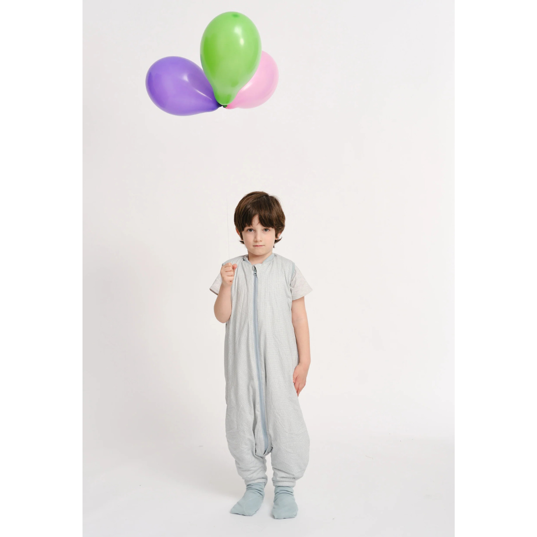 Criança com saco de dormir cinzento segurando balões coloridos