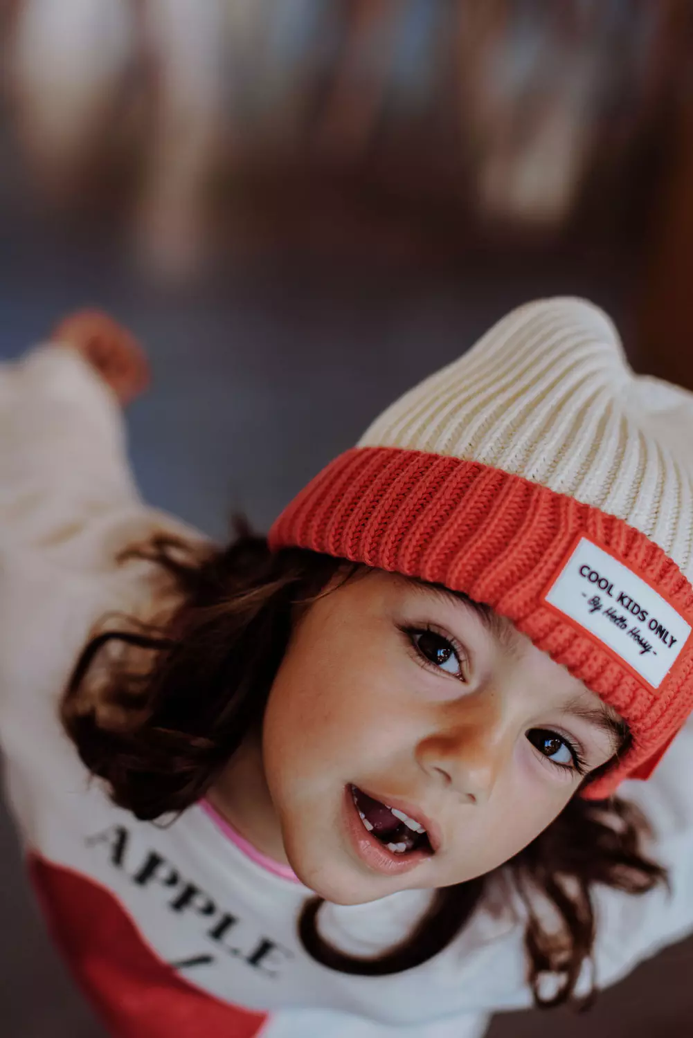 Criança com chapéu de malha creme e vermelho com etiqueta COOL KIDS ONLY e camisola branca com texto