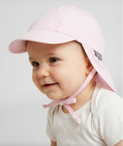 Bebé de chapéu cor-de-rosa com pala e proteção traseira, fita para atar e t-shirt branca