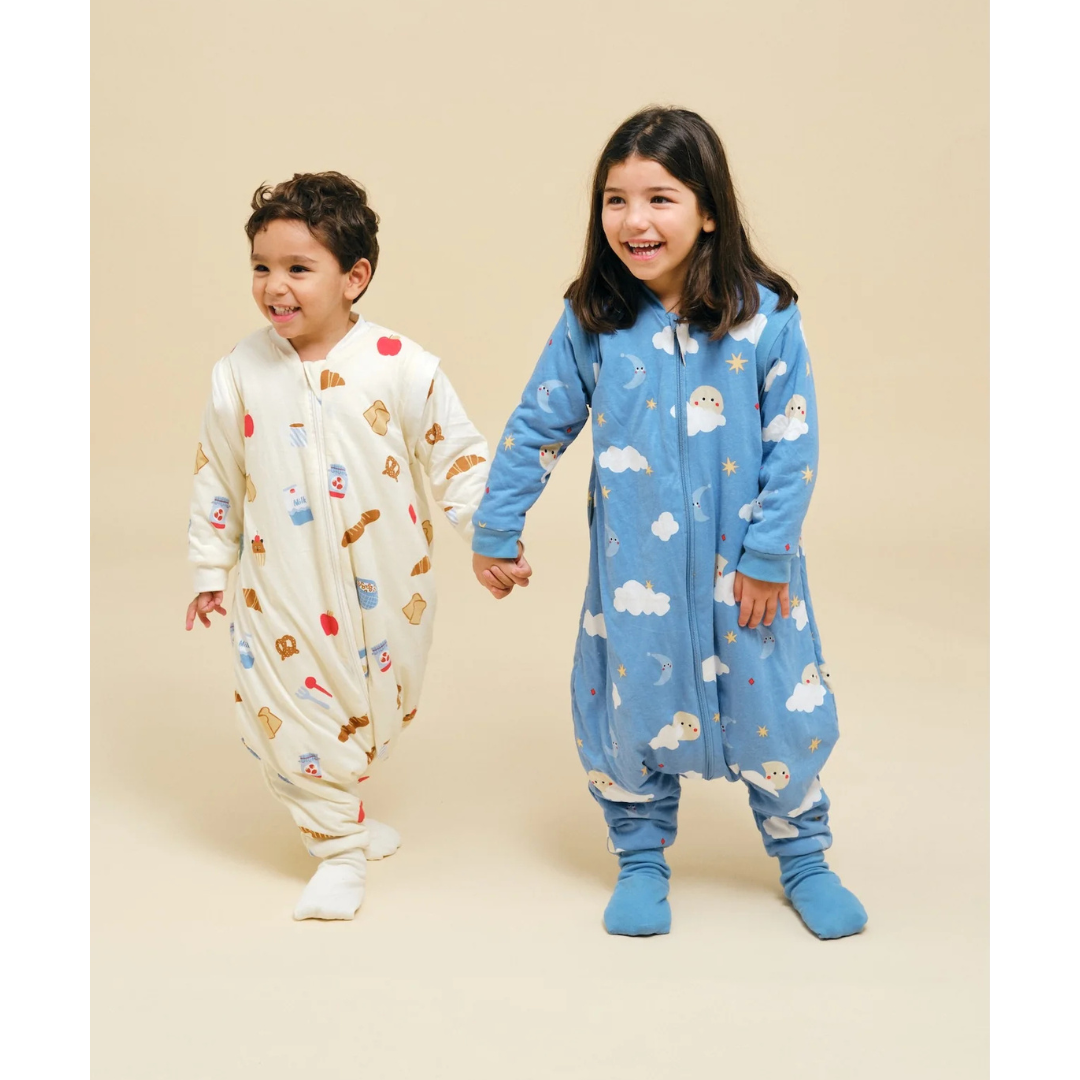 Crianças de pijamas com estampados temáticos, mão na mão, em fundo neutro.