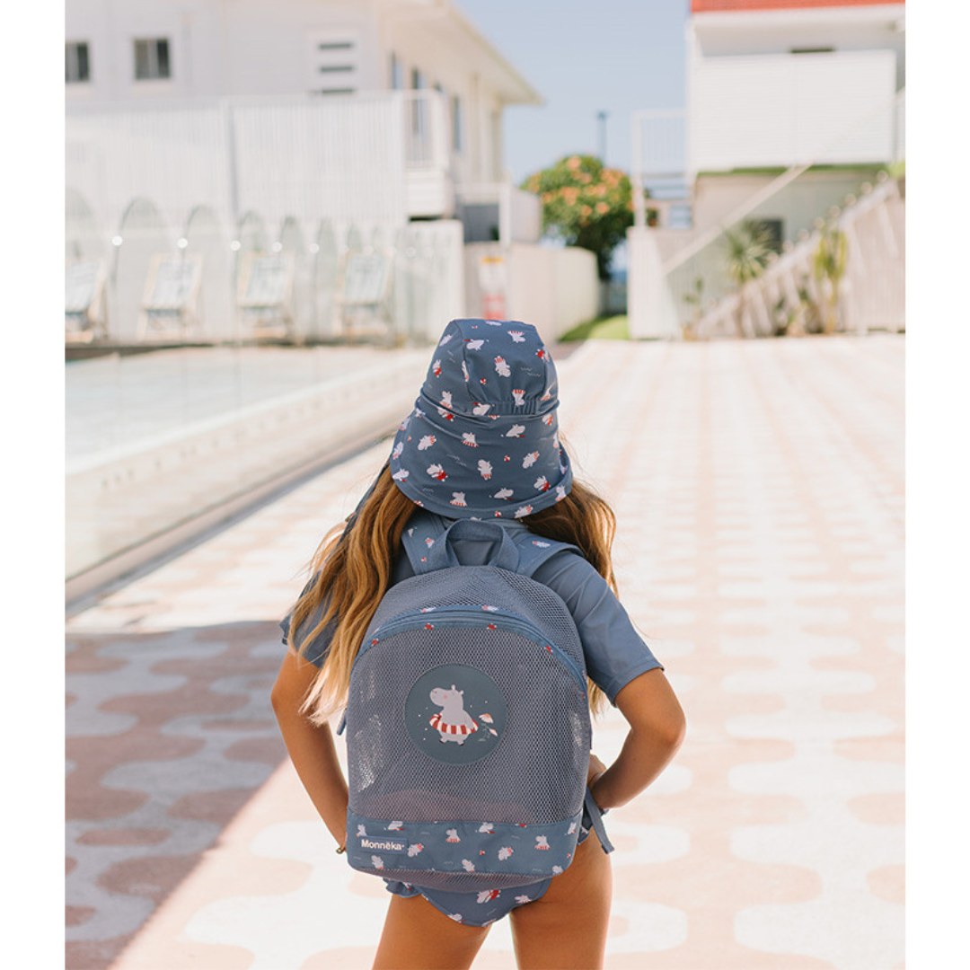 Criança com mochila e chapéu padrões hipopótamos azuis ao lado de piscina