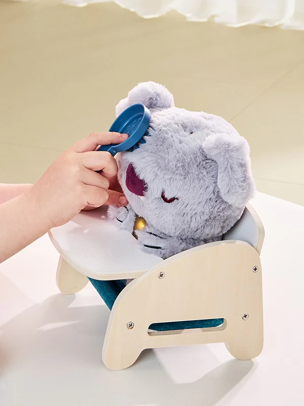 Boneco de pelúcia cinzento sentado numa cadeira infantil em madeira clara.