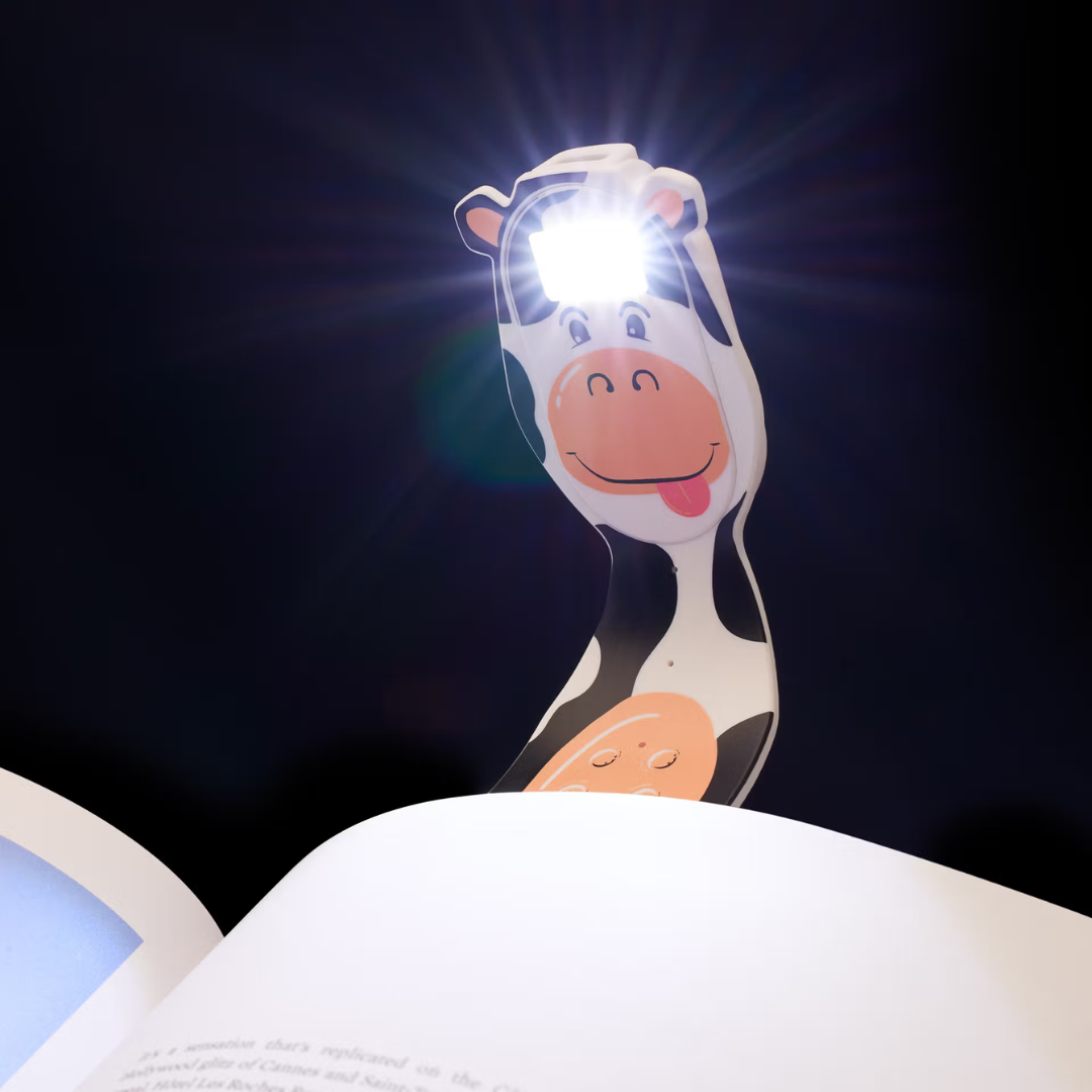 Lâmpada de leitura em forma de vaca com luz no rosto junto a um livro aberto