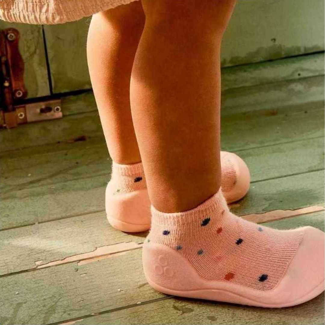 Meias-sapato cor-de-rosa com padrão de pontos coloridos em chão de madeira verde