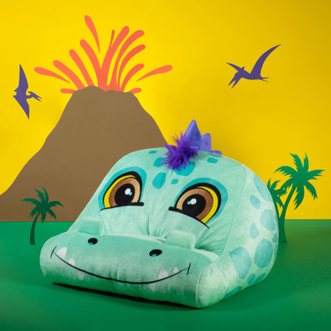 Almofada azul claro formato cabeça de dinossauro com crista roxa, olhos grandes e fundo com vulcão desenhado.