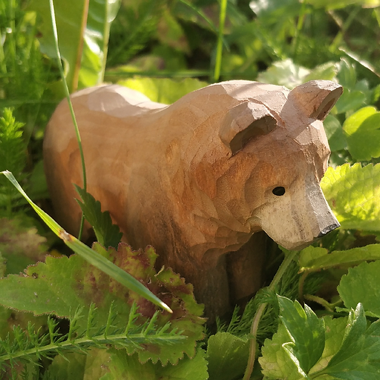 Escultura de madeira rústica de um urso marrom entre folhas verdes