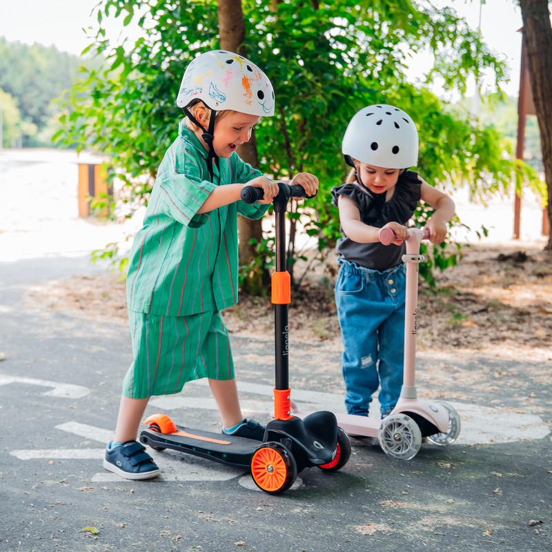 Crianças a andar de trotinetes três rodas com capacetes em área exterior com árvores