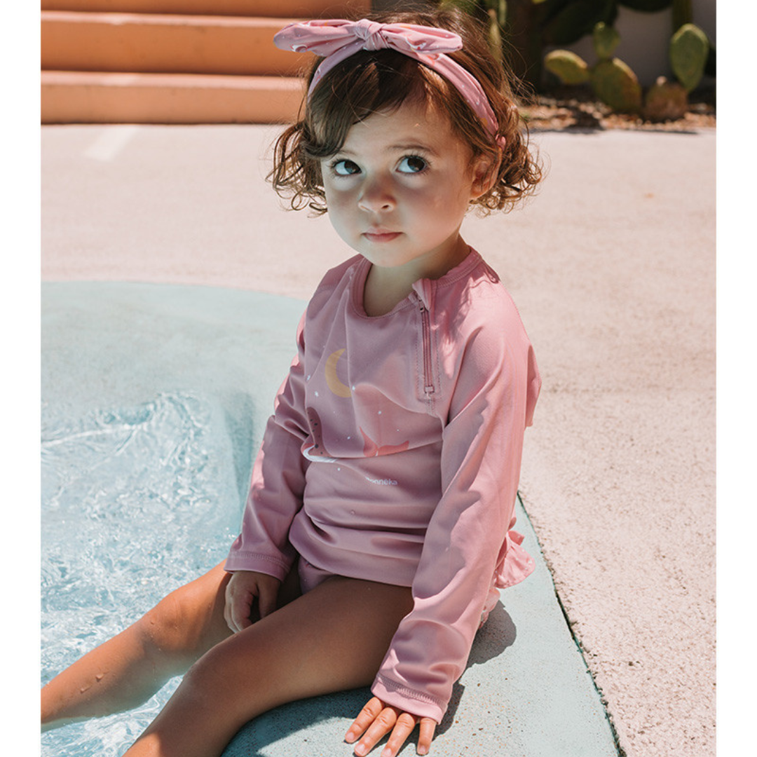 Criança com roupa de banho rosa e faixa de cabelo sentada na borda da piscina