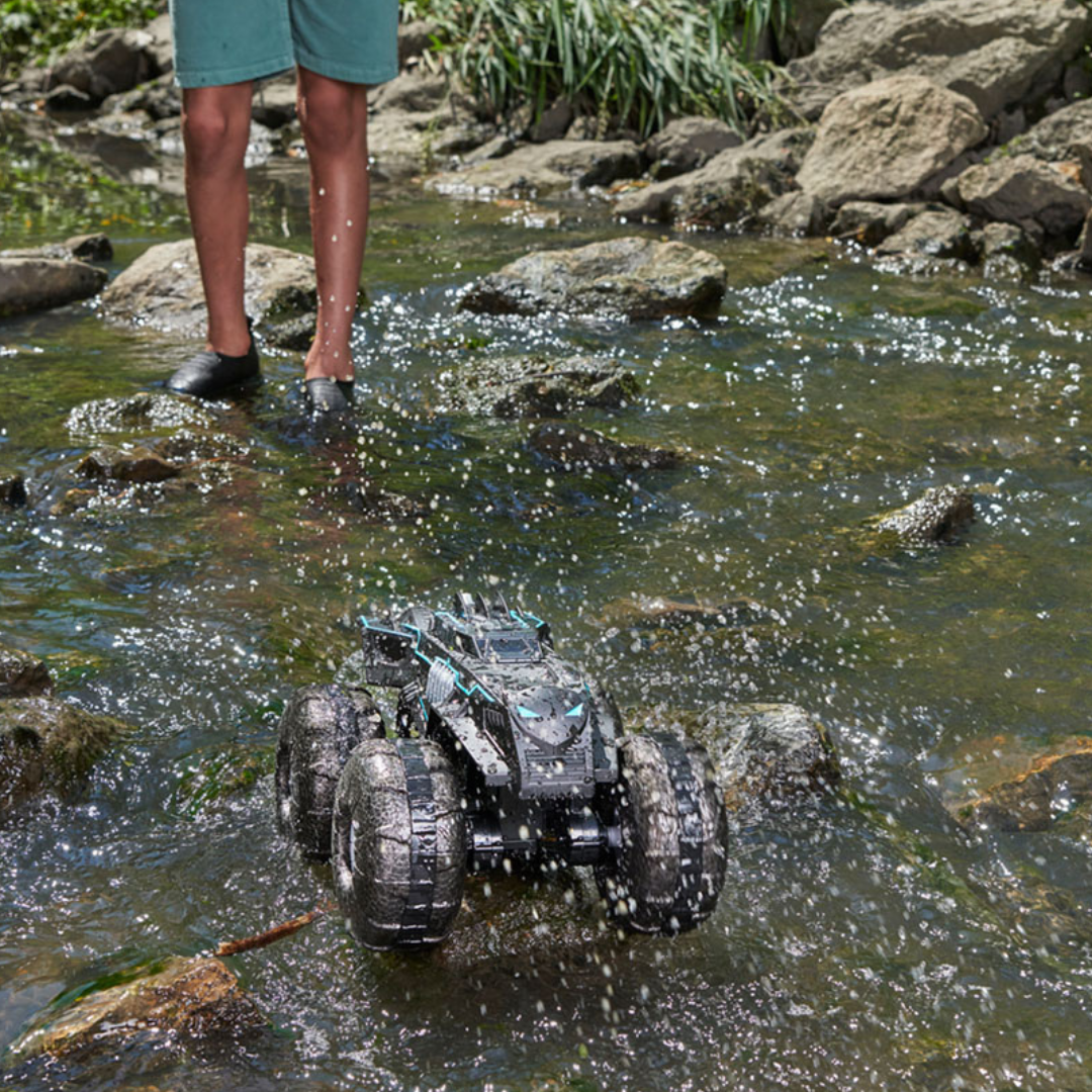 Veículo de controlo remoto preto e azul em água rasas entre pedras com pessoa ao fundo