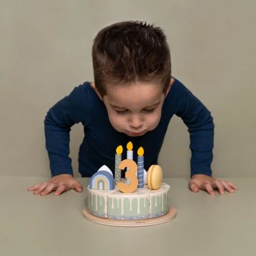 Criança com camisola azul escura sopra velas num bolo com vela número 3 e decoração colorida