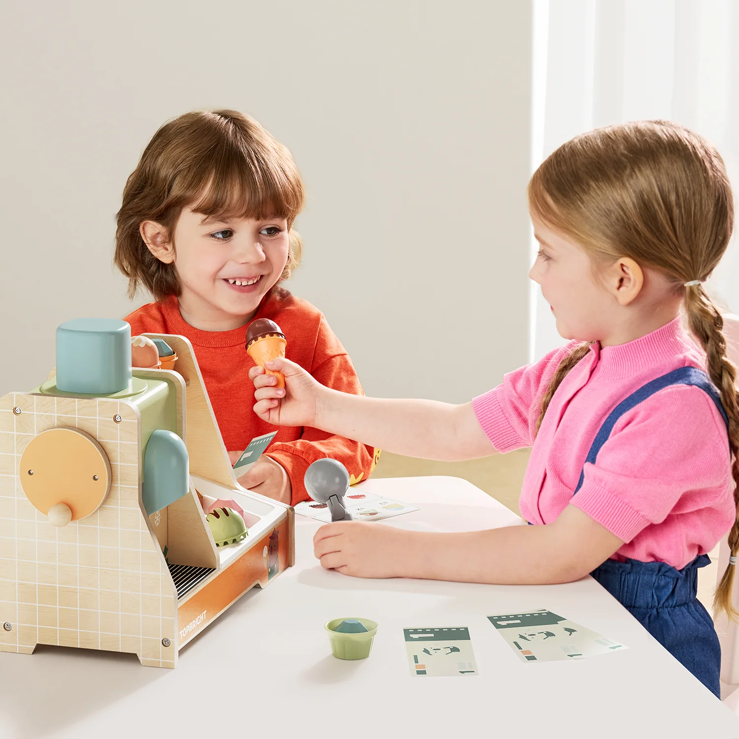 Crianças a brincar com caixa registadora de madeira e gelados de brinquedo.