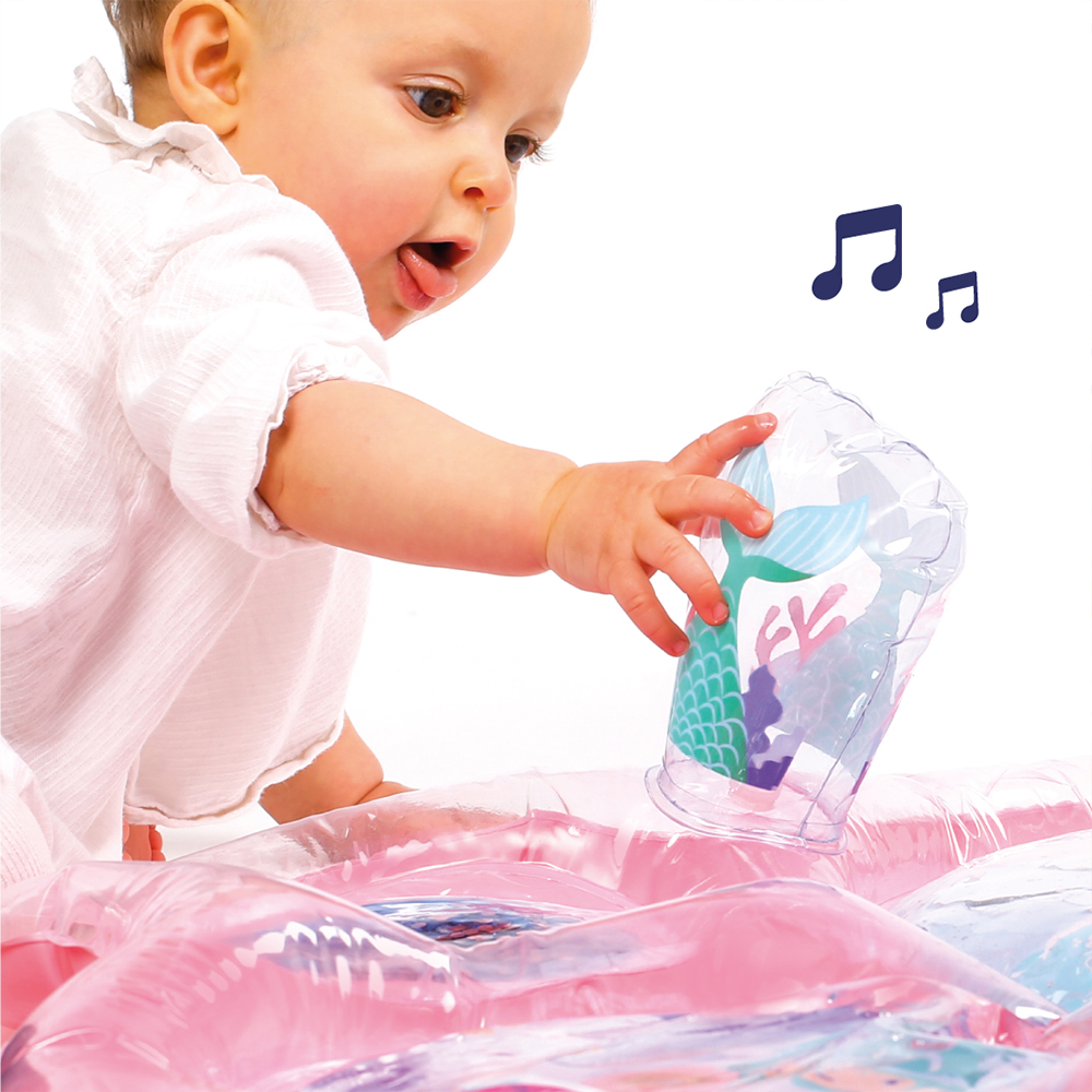 Bebé de camisa branca segurando copo com desenho de cauda de sereia junto a piscina insuflável cor-de-rosa.