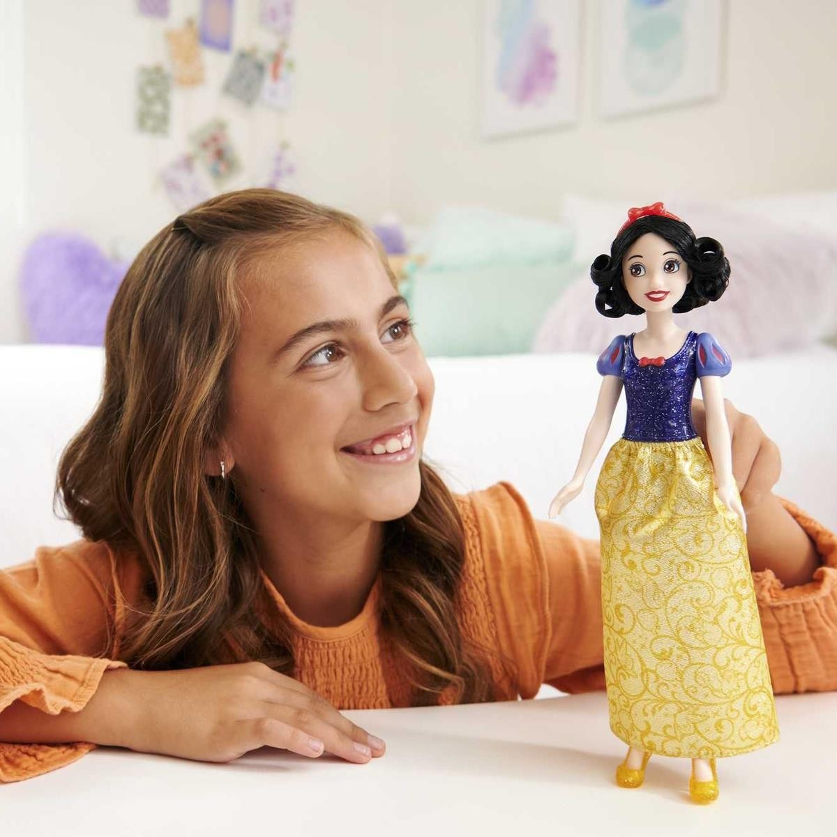 Boneca da princesa Branca de Neve com vestido azul e amarelo com padrão dourado em cima de mesa branca, criança sorridente ao lado