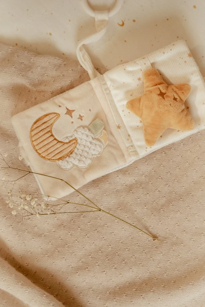 Livro de tecido para bebé com estrelas e lua bordadas, e uma estrela de peluche laranja