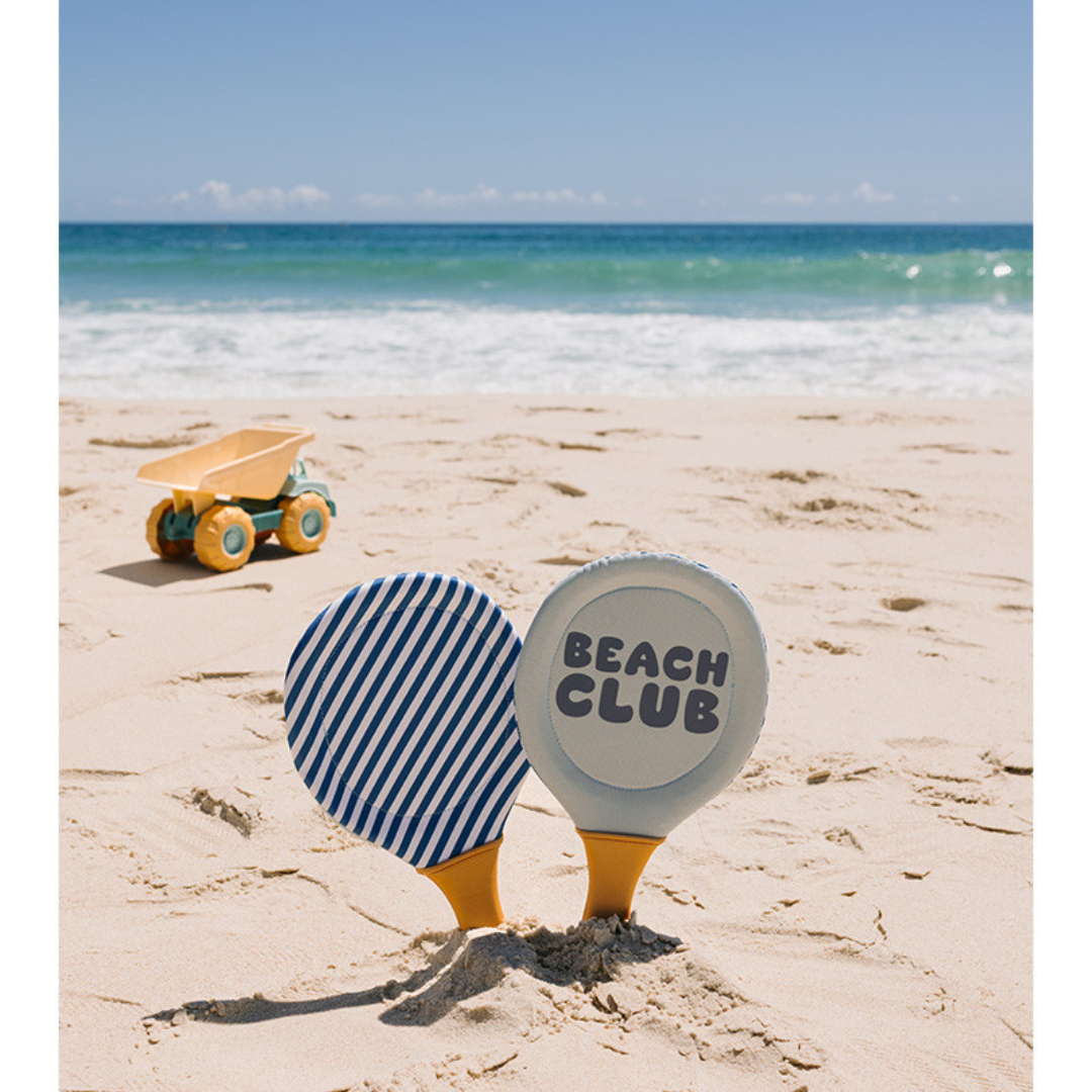 Raquetes de praia coloridas na areia junto a carrinho de brinquedo e mar ao fundo