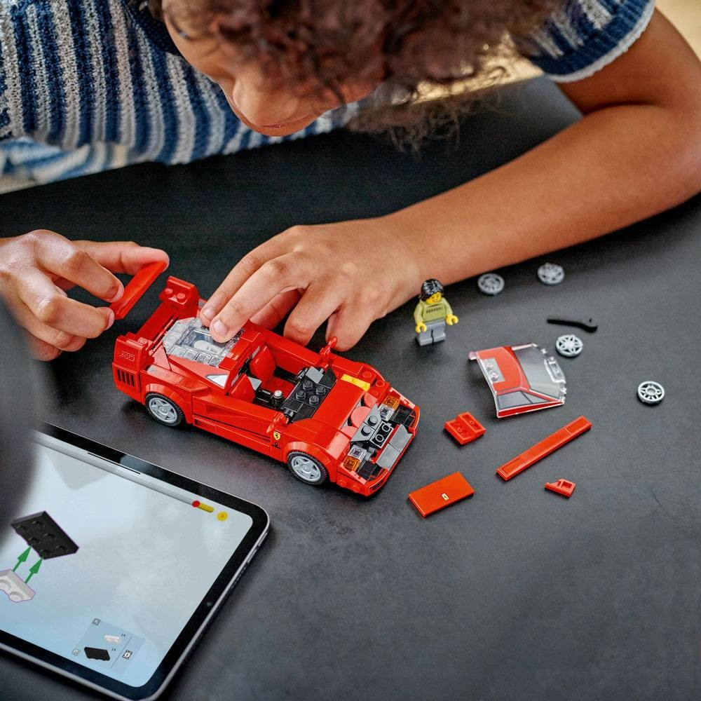 Criança montando um carro de LEGO vermelho com peças e tablet ao lado