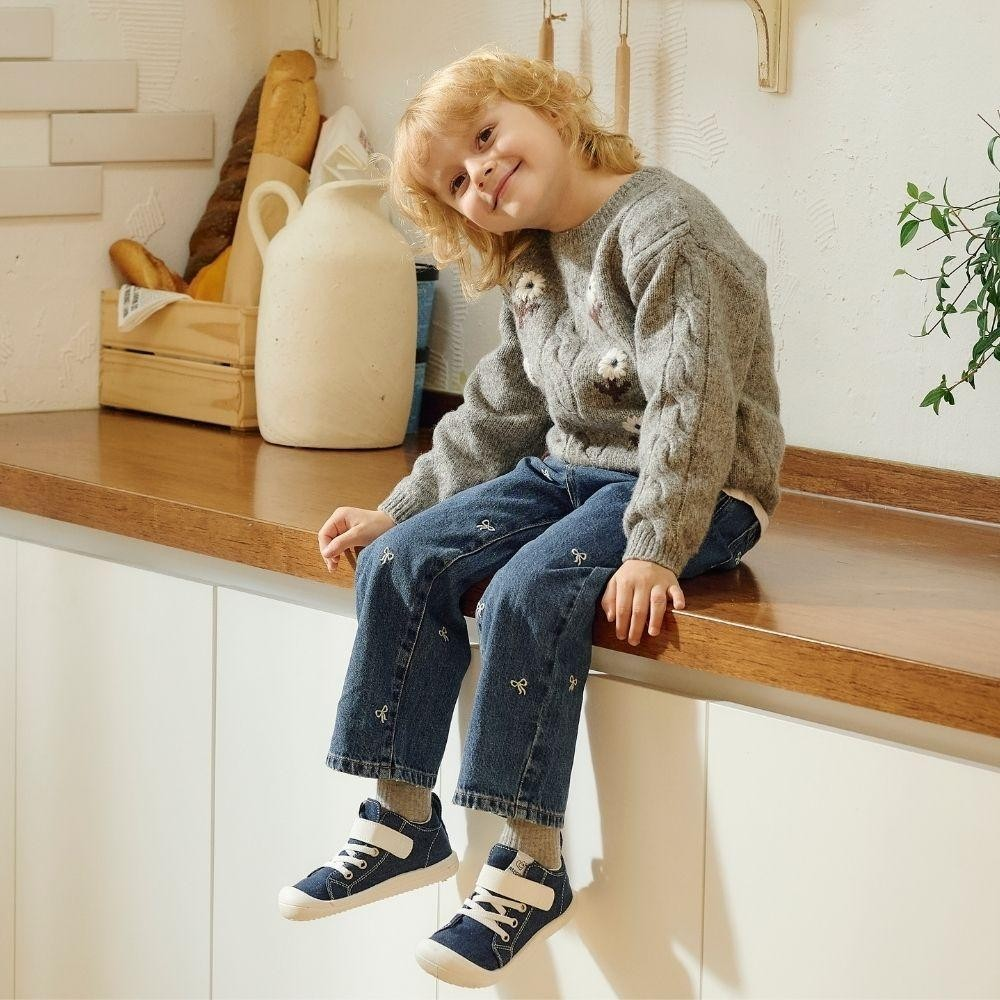 Criança sentada numa bancada de cozinha com roupa casual e sapatilhas