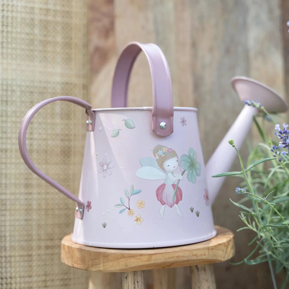 Regador de metal cor-de-rosa claro com ilustração de fada e flores sobre banco de madeira