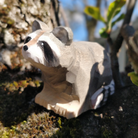 Figura de guaxinim em madeira sobre musgo e tronco