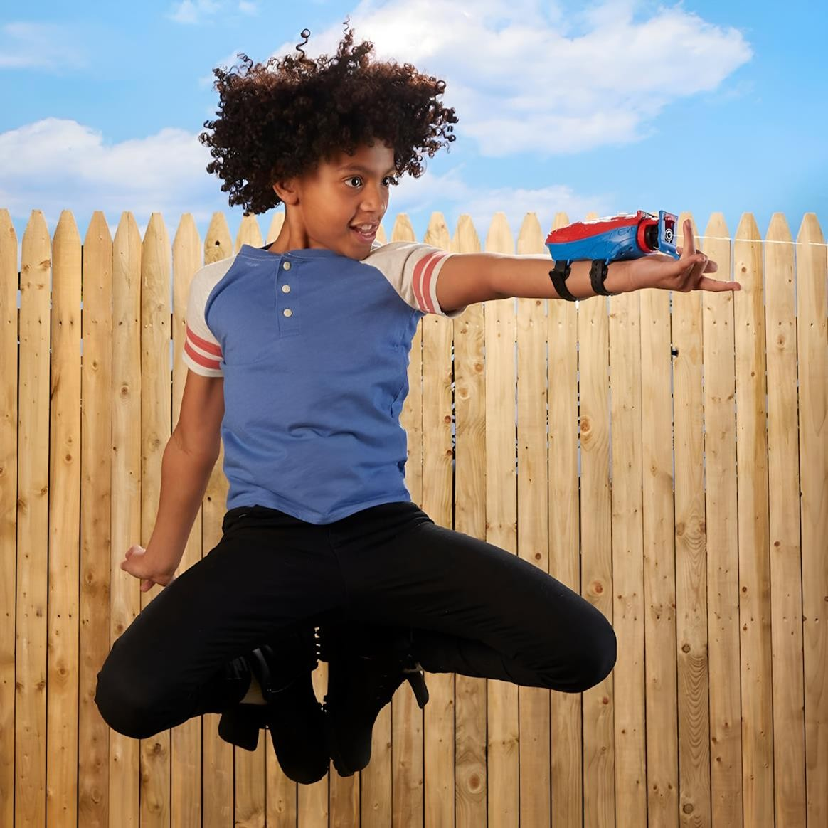 Criança com brinquedo lançador de água a saltar em frente a vedação de madeira