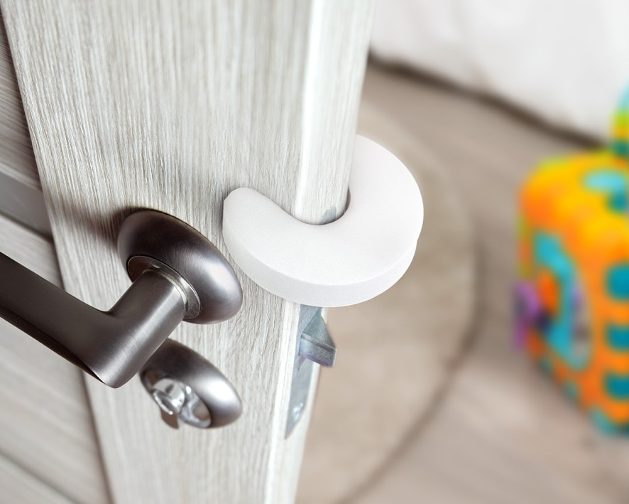 Protetor branco colocado na borda de porta de madeira clara com maçaneta metálica escura