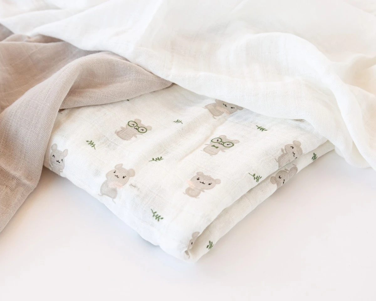 Lençol ou fralda branca e bege com padrão de ursinhos cinza claro encostado numa superfície branca.
