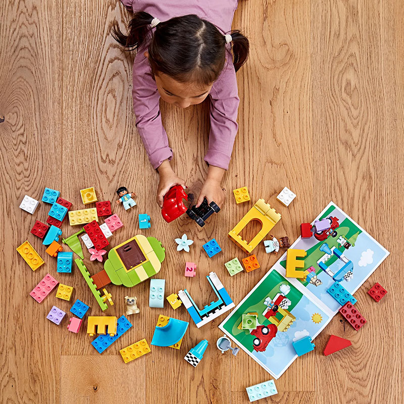 Criança a brincar com peças de Lego coloridas em chão de madeira clara