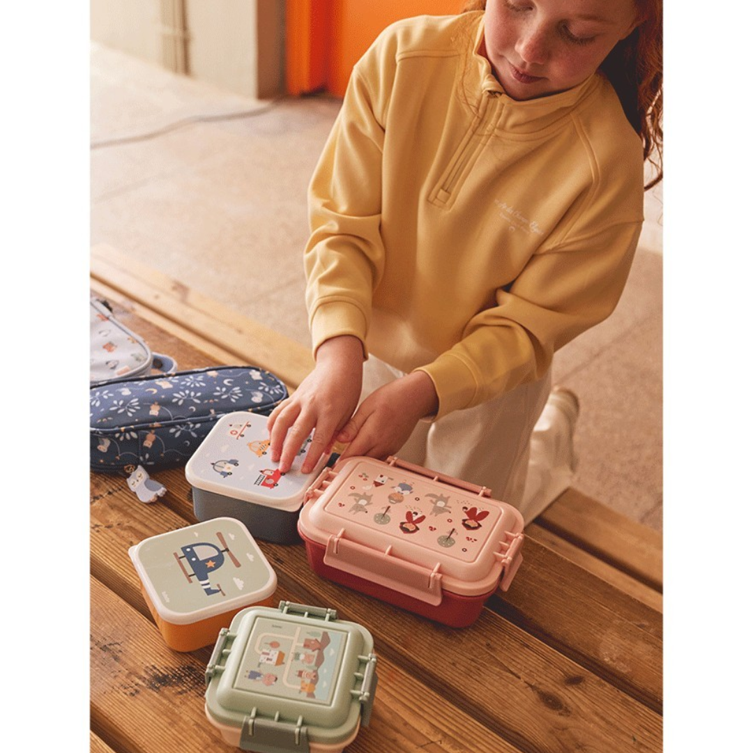 Criança a abrir caixas de merenda coloridas com desenhos de animais sobre mesa de madeira
