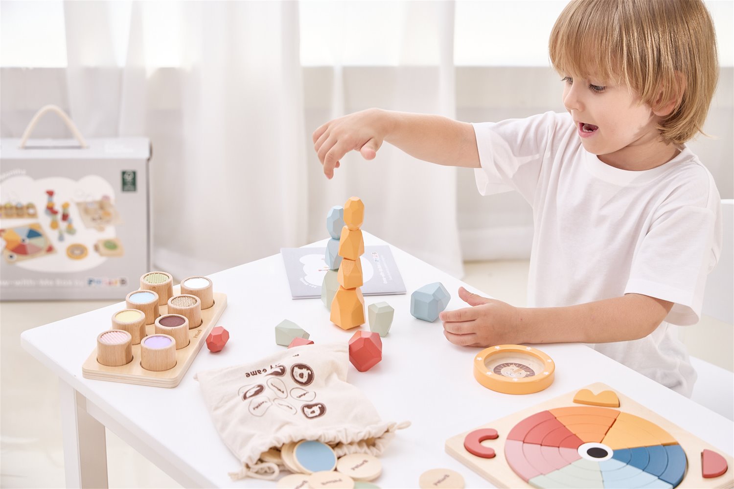 Criança a brincar com brinquedos educativos em madeira coloridos numa mesa branca