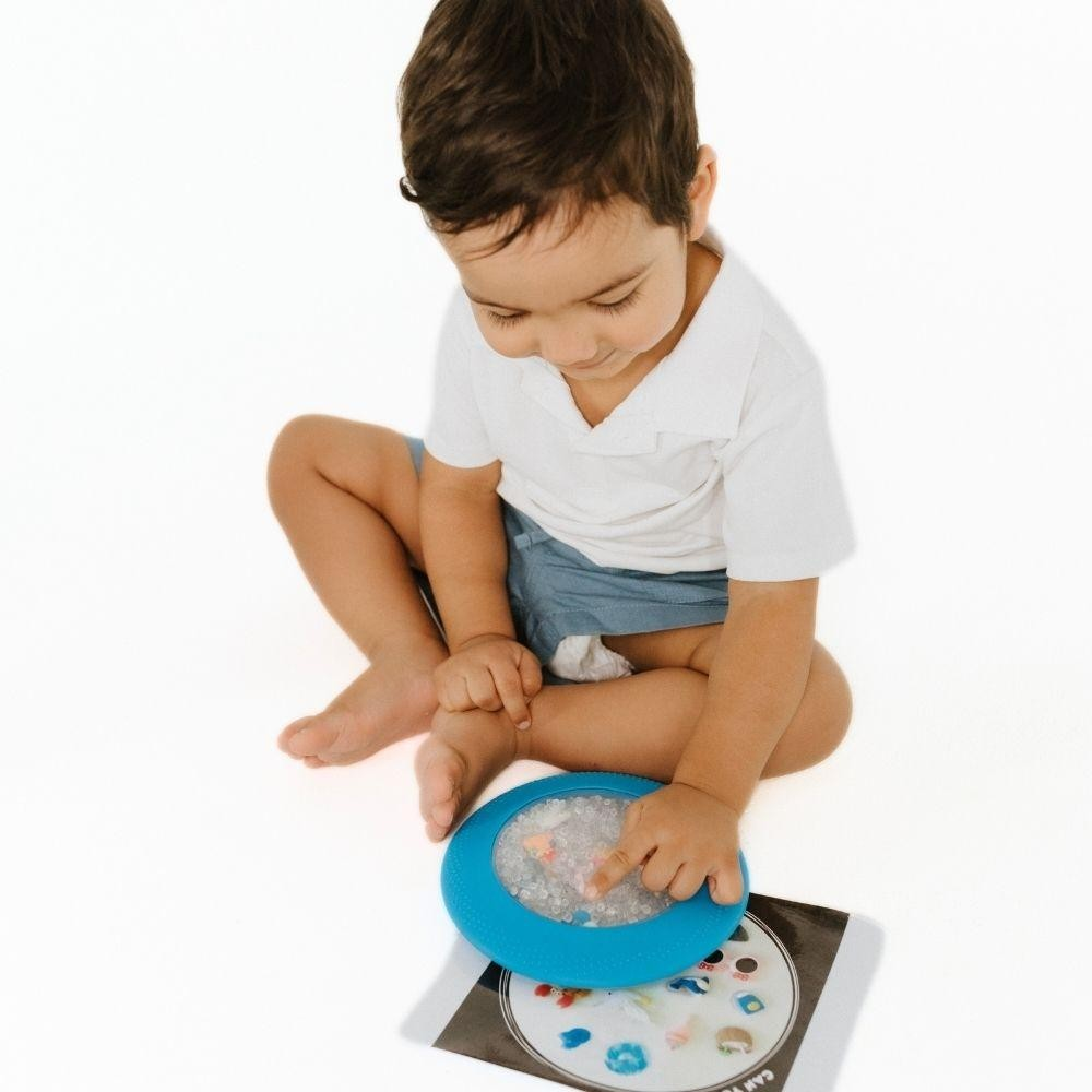 Criança a brincar com brinquedo azul e livro no chão branco