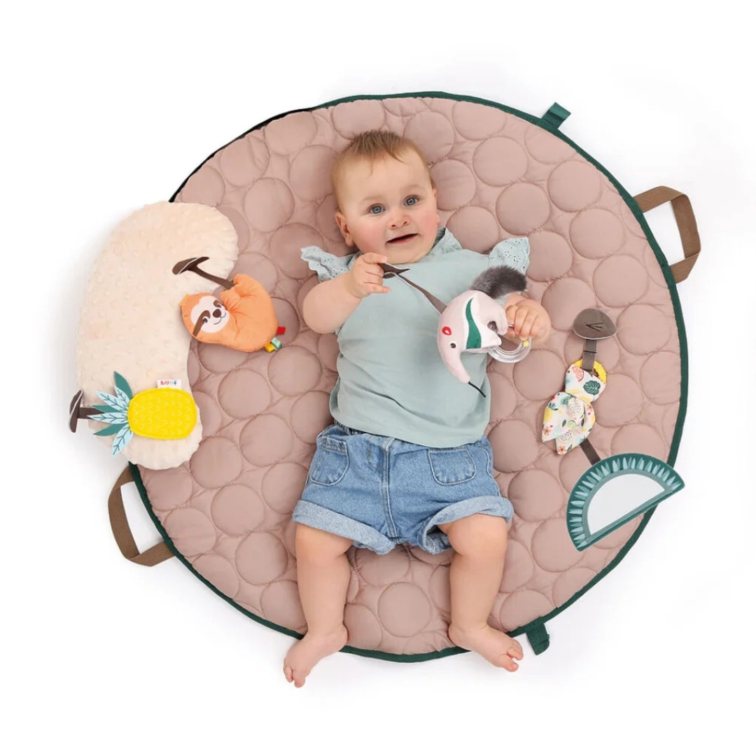 Bebé deitado em tapete redondo cor de rosa com brinquedos coloridos