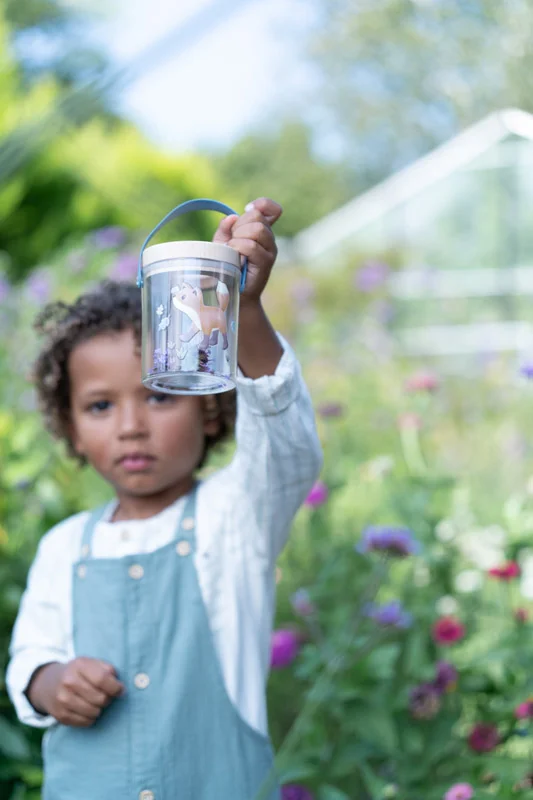 Criança segura frasco transparente com brinquedos em jardim colorido