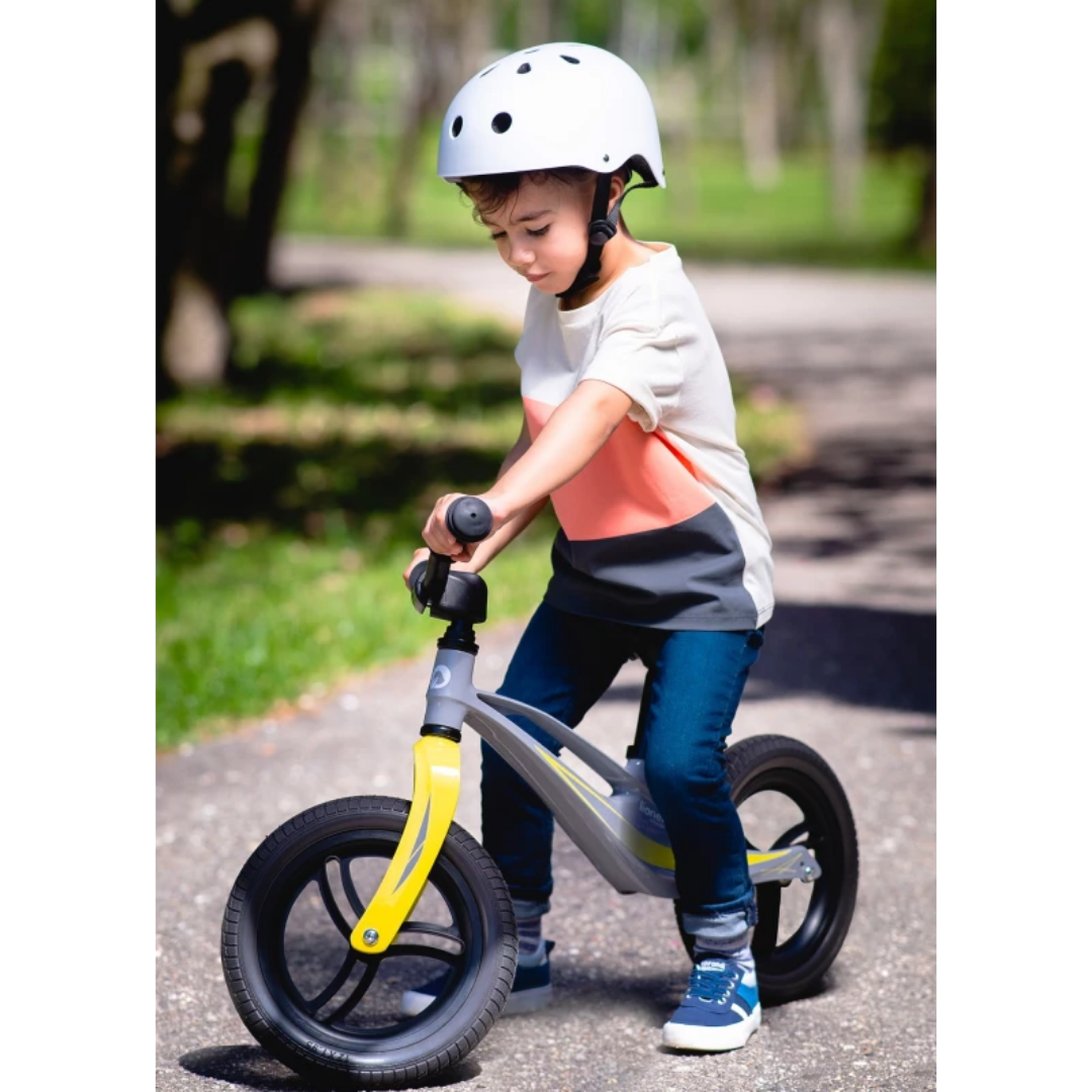 Criança com capacete branco numa bicicleta sem pedais cinzenta e amarela ao ar livre