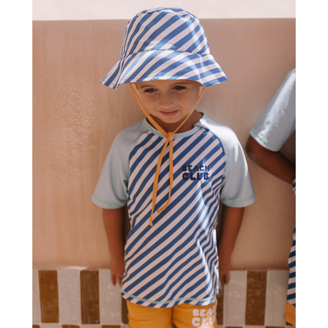 Criança com roupa de praia azul e branca com texto BEACH CLUB